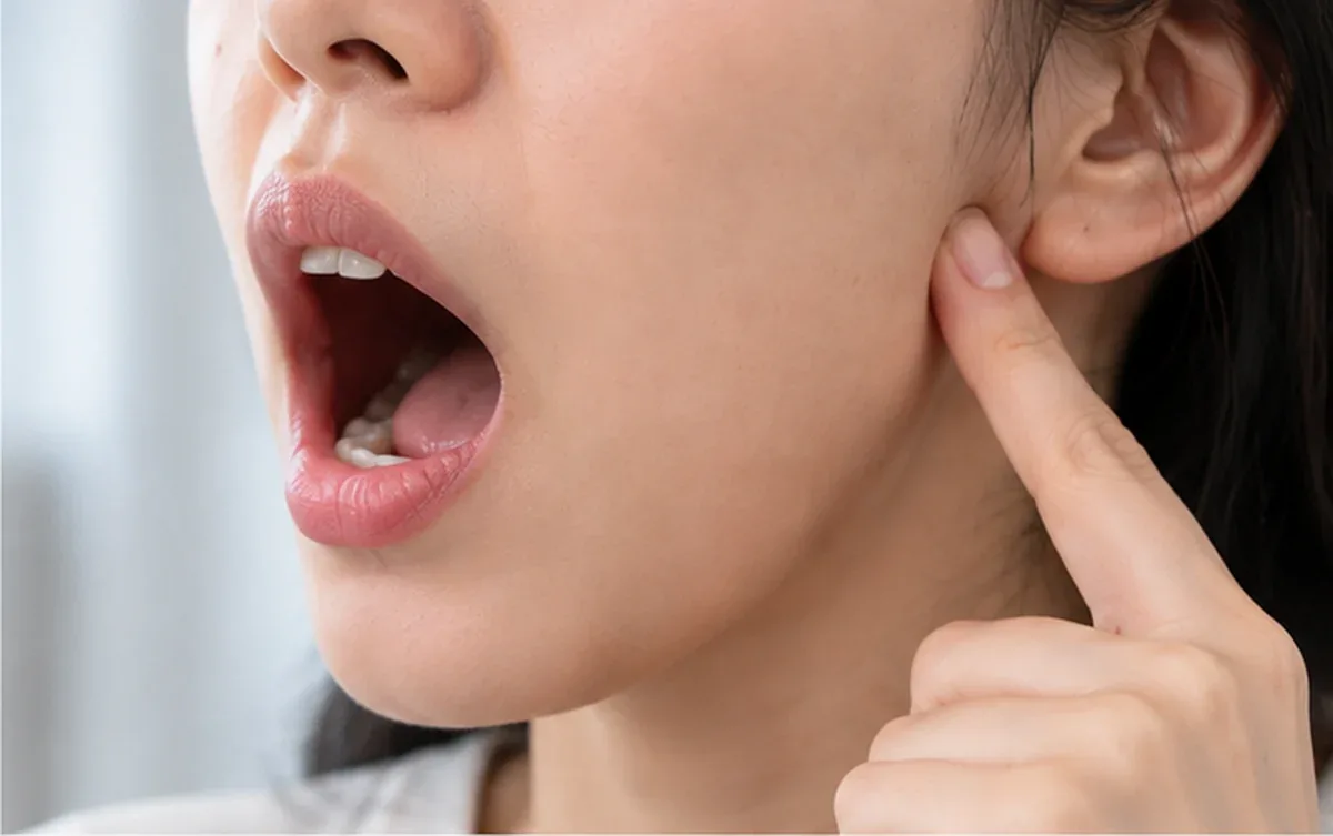입을 크게 벌리면서 귀 바로 앞 턱 관절 자리를 손가락으로 짚어 보는 모습 — 리셋치과의원