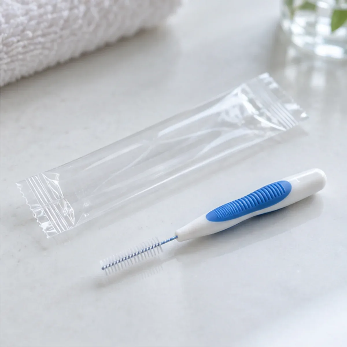 밝은 탁자 위에 치간칫솔 한 개와 투명한 포장지가 나란히 놓인 모습 — 리셋치과의원
