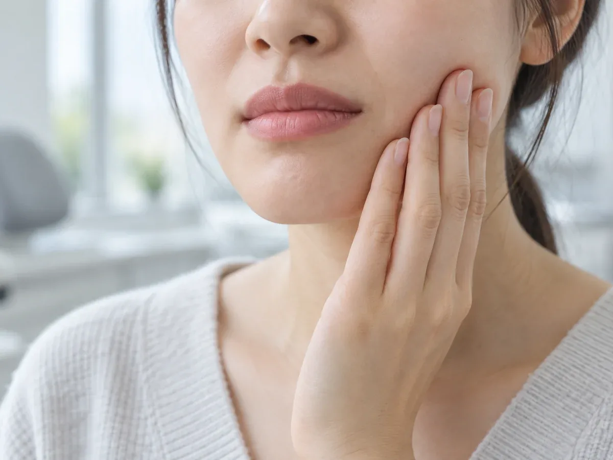 치과 치료를 받은 뒤 한쪽 볼을 손으로 짚고 있는 사람의 모습 — 리셋치과의원